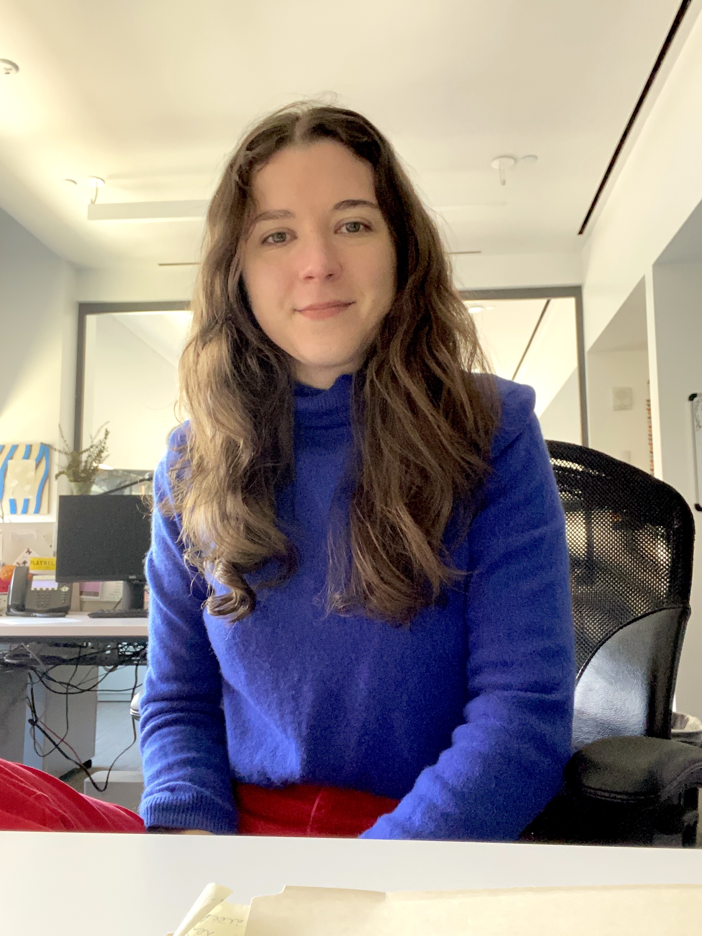 Portrait of Martha Tenney (a white woman with brown hair and a purple sweater sits in an office chair with an office seen behind her)
