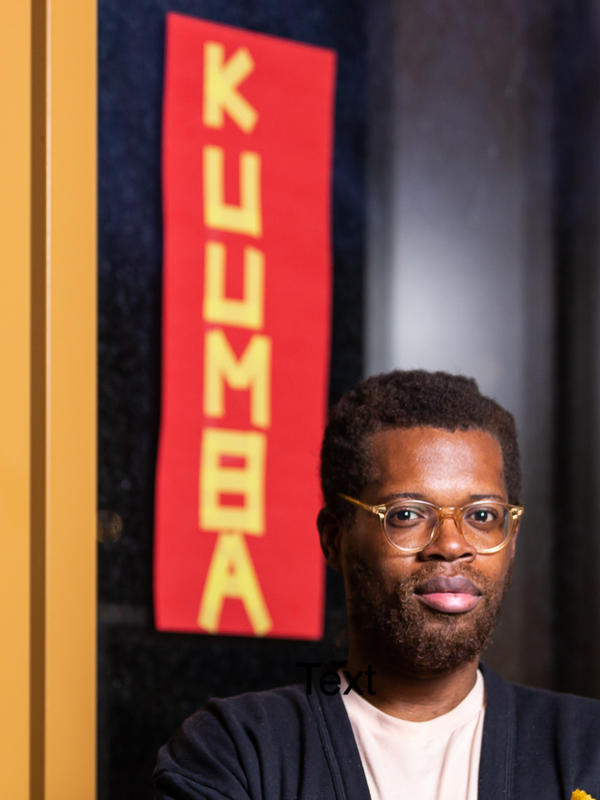 Obden Mondésir in front of a red flag that reads Kuumba